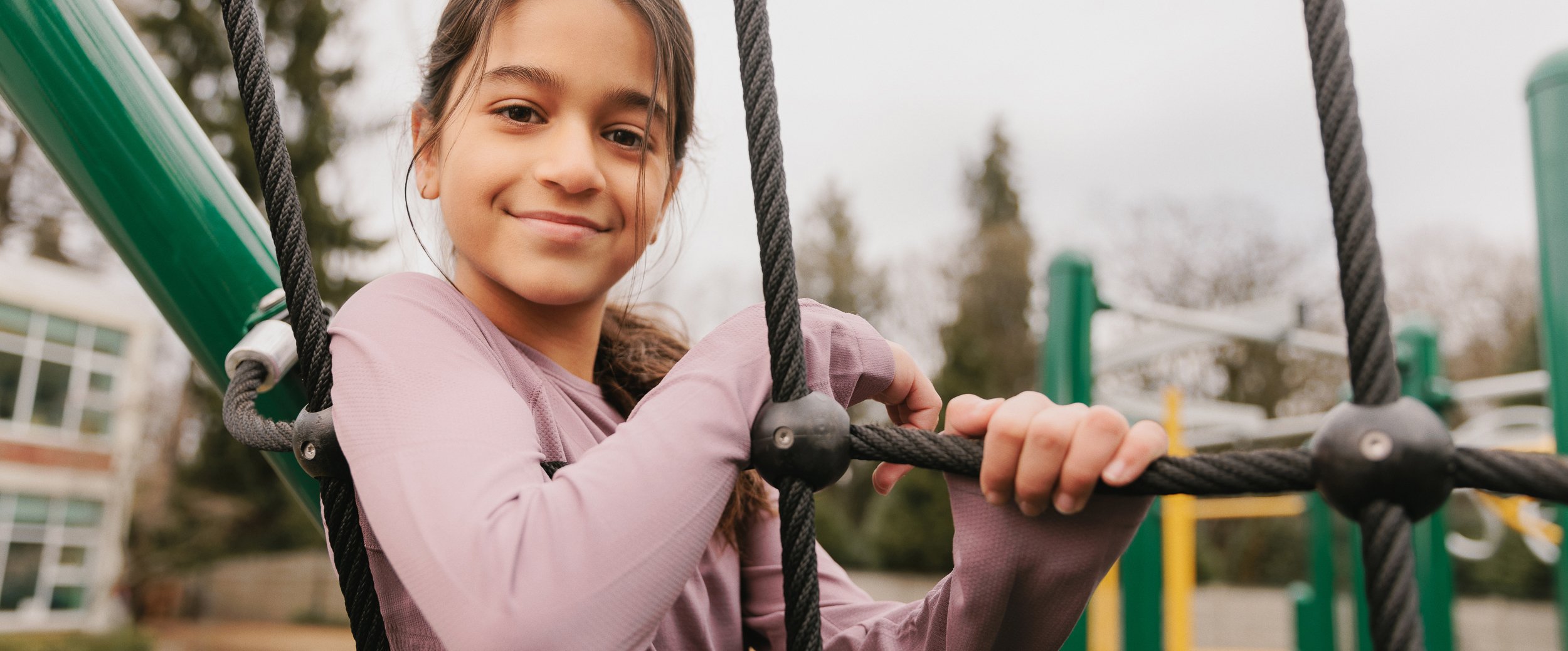 Girl resting against a climbing rope smiling at camera.